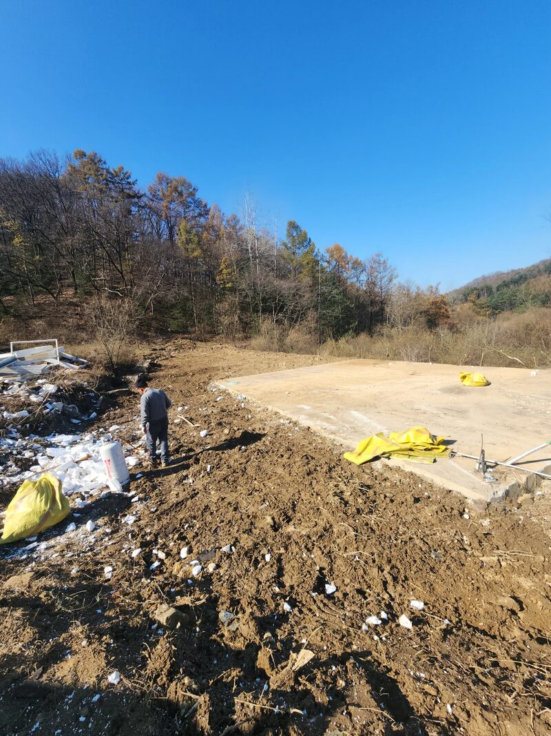 용인판넬창고철거 현장 - 콘크리트 기초 슬래브와 판넬 잔재가 남은 부지에 작업자가 멀리 서 있는 모습